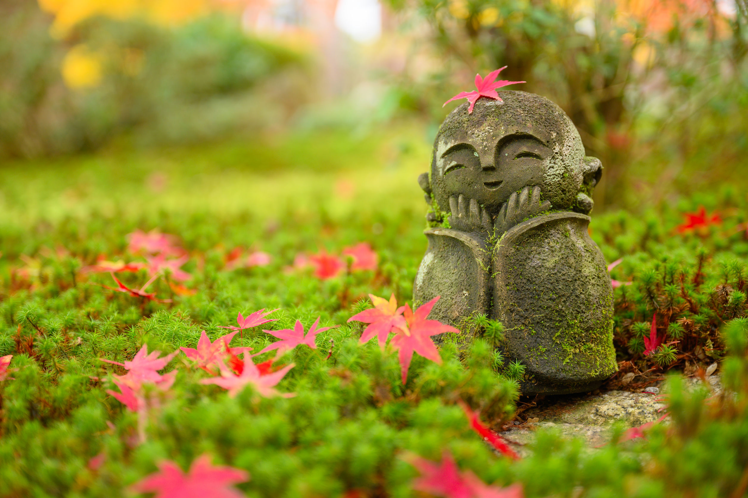 Feuille d'érable sur une petite sculpture de moine dans un jardin japonais