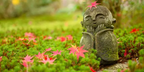 Feuille d'érable sur une petite sculpture de moine dans un jardin japonais